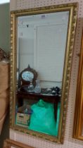 A gilt framed narrow oblong wall mirror with bevelled plate and decorative border