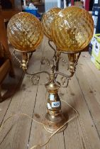 A vintage brass three branch table lamp with ceramic bosses, depicting hunting scenes and three