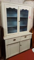 A 1,2m white painted wood two part dresser with shelves enclosed by a pair of glazed panel doors,