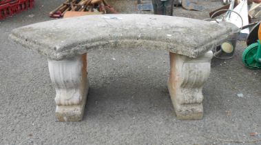 A concrete garden bench of curved form, set on shaped supports