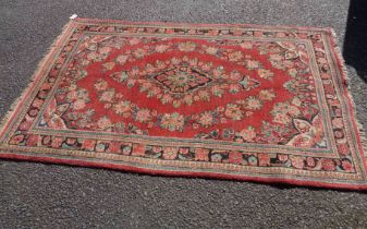 A vintage handmade wool rug with central floral motifs and swags within a wide border on red