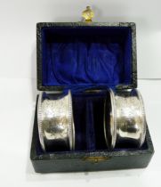 A cased pair of silver napkin rings with engraved foliage and beaded rims