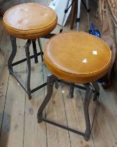 A pair of reproduction industrial style adjustable stools with upholstered tan leather seats, set on