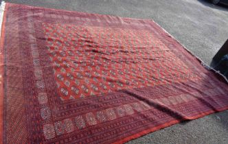A Bokara handmade wool carpet with repeat motifs within a triple border on red ground - moth
