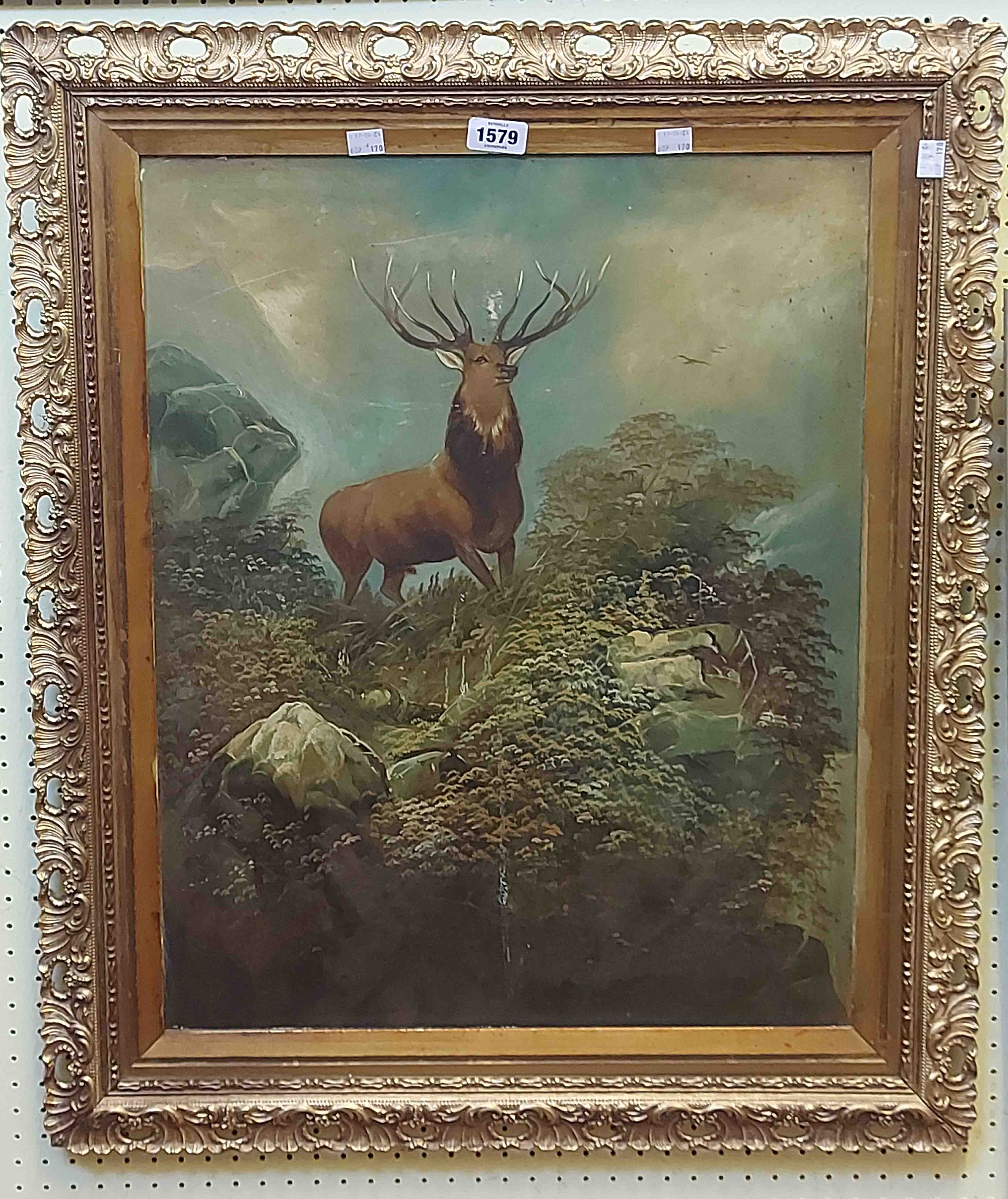 An ornate gilt framed early 20th Century oil on card, depicting a stag standing on a rocky outcrop -