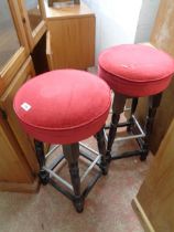 A pair of modern stained wood bar stools with red upholstered seats, set on turned supports