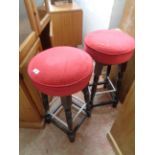 A pair of modern stained wood bar stools with red upholstered seats, set on turned supports