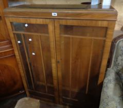 A 94cm 1930's walnut veneered display cabinet enclosed by a pair of glazed panel doors, set on