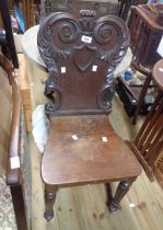 A Victorian mahogany hall chair with ornate carved back and solid seat, set on reeded front legs
