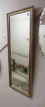 A gilt framed narrow bevelled oblong wall mirror with decorative border