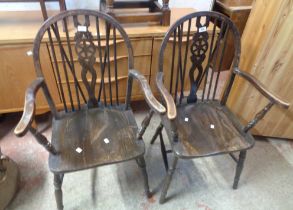 A pair of vintage stained oak wheelback carver chairs with moulded solid seats, set on turned