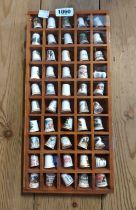 A small wooden display shelf containing a quantity of ceramic thimbles