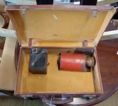 A small brown suitcase containing a vintage box Brownie camera and a metal part projector