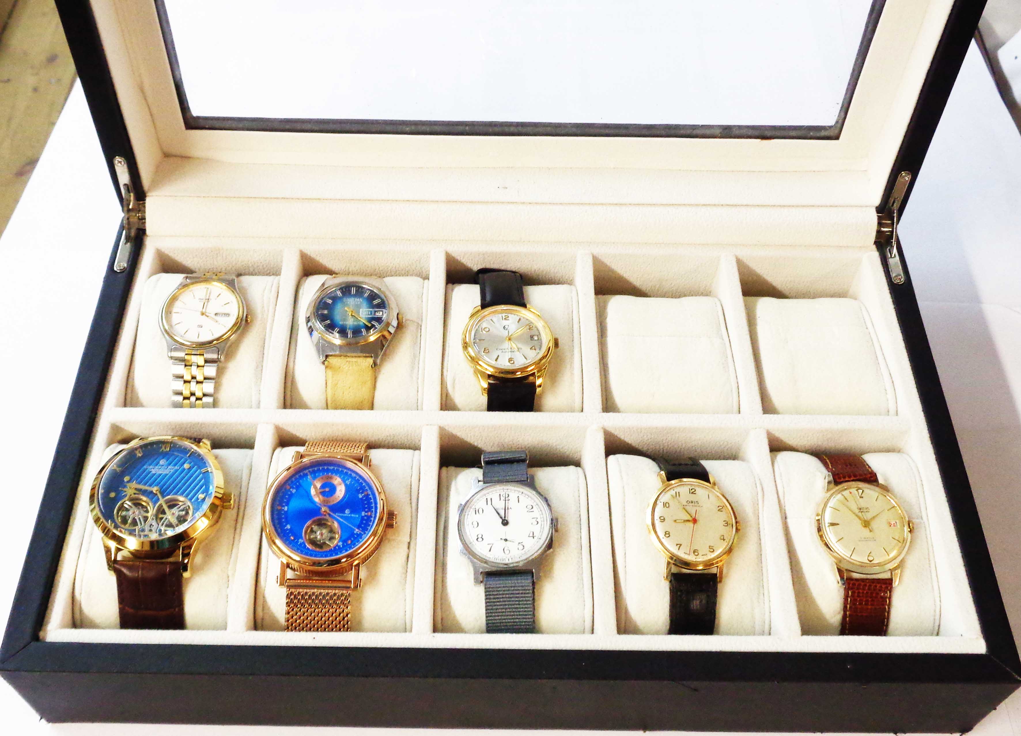 An upholstered perspex topped watch display case containing a collection of eight vintage and modern