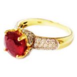 A marked 10k ring, set with central circular heat treated ruby with tiny diamonds to shoulders -