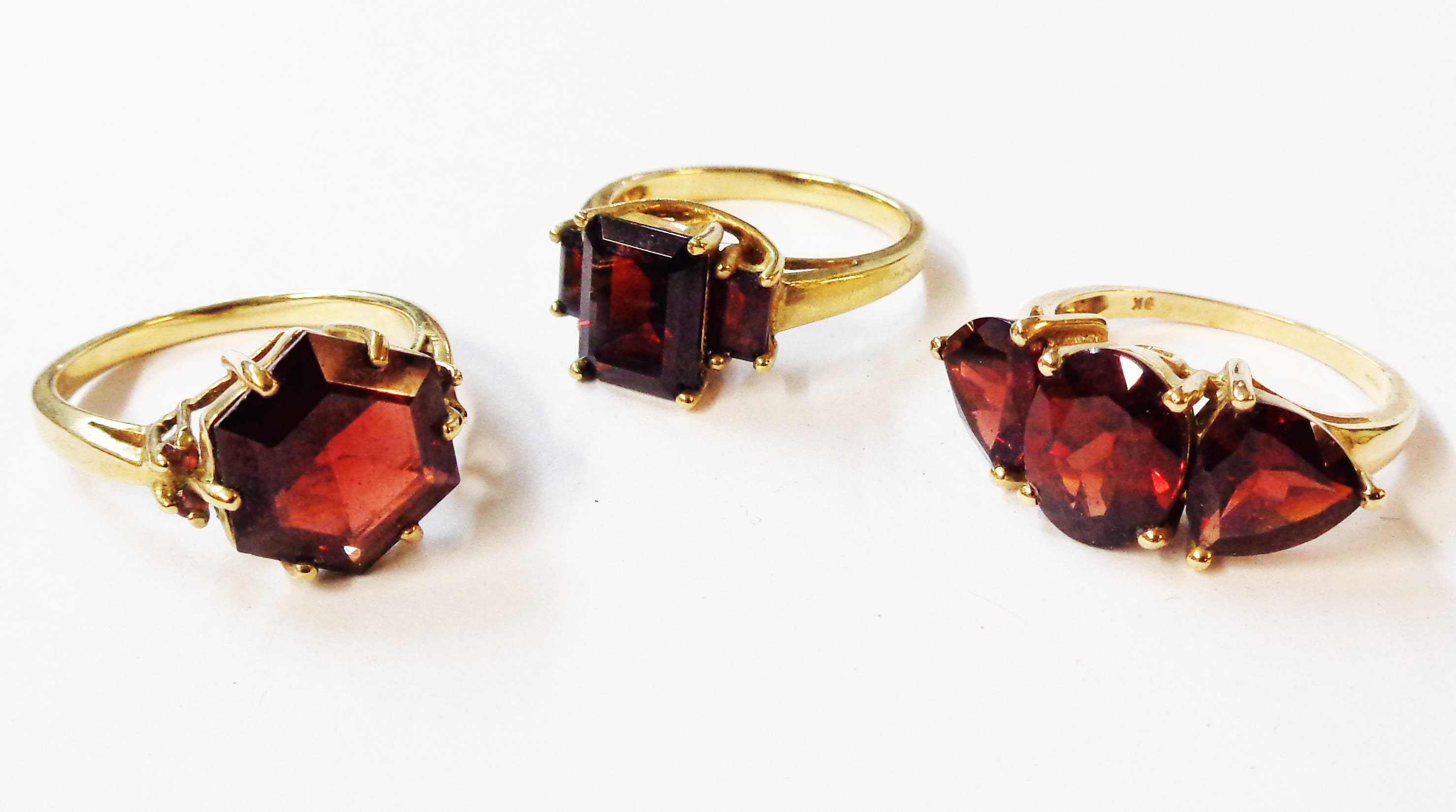 Three 375 (9ct.) gold rings, all set with various garnets comprising a solitairre, three stone and