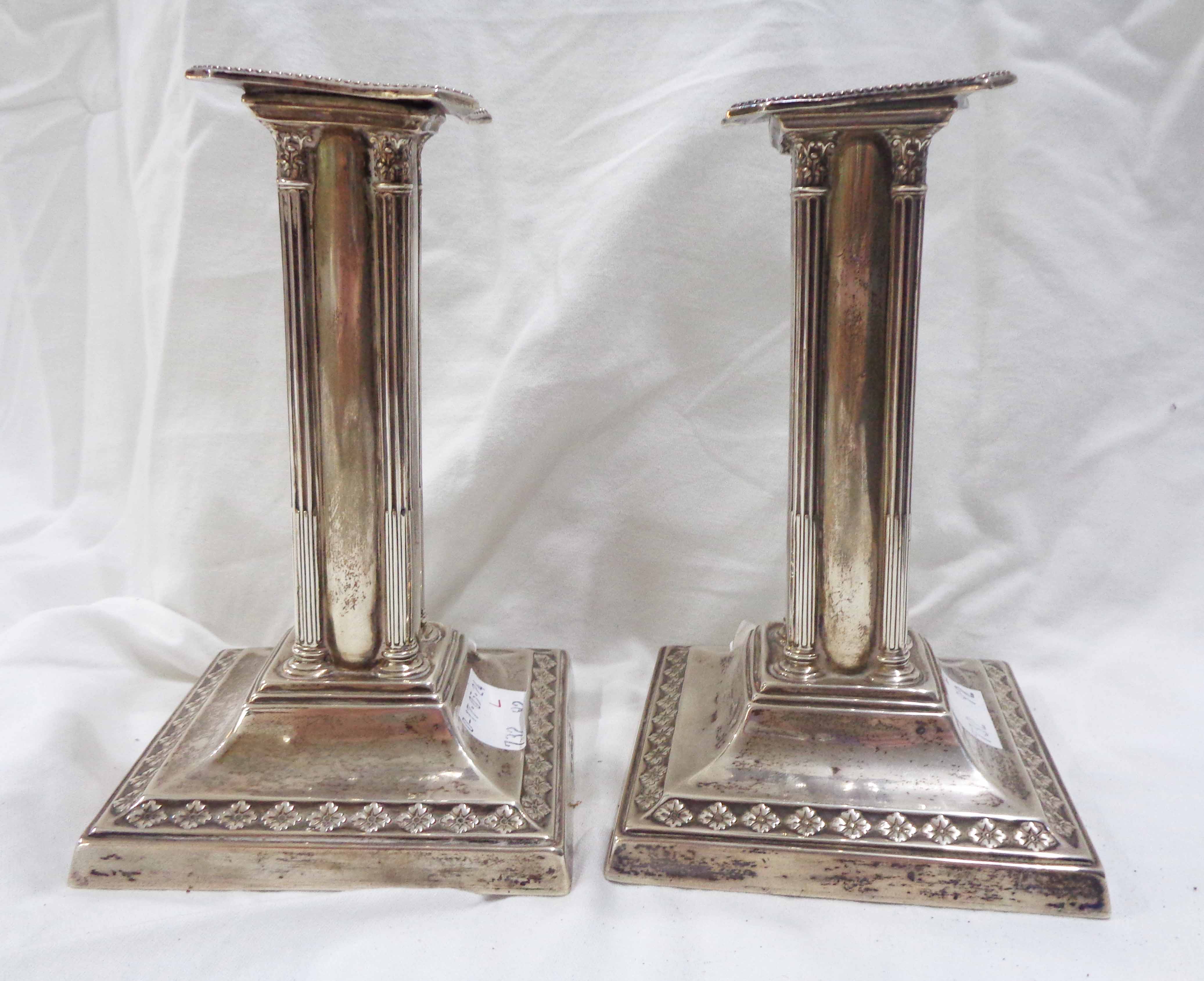 A pair of 12.5cm high silver candlesticks of column form with embossed decoration - one base loading