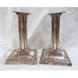 A pair of 12.5cm high silver candlesticks of column form with embossed decoration - one base loading