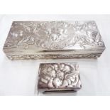 An 18cm silver oblong box with embossed cherub group and foliate scrolls to the hinged lid and sides