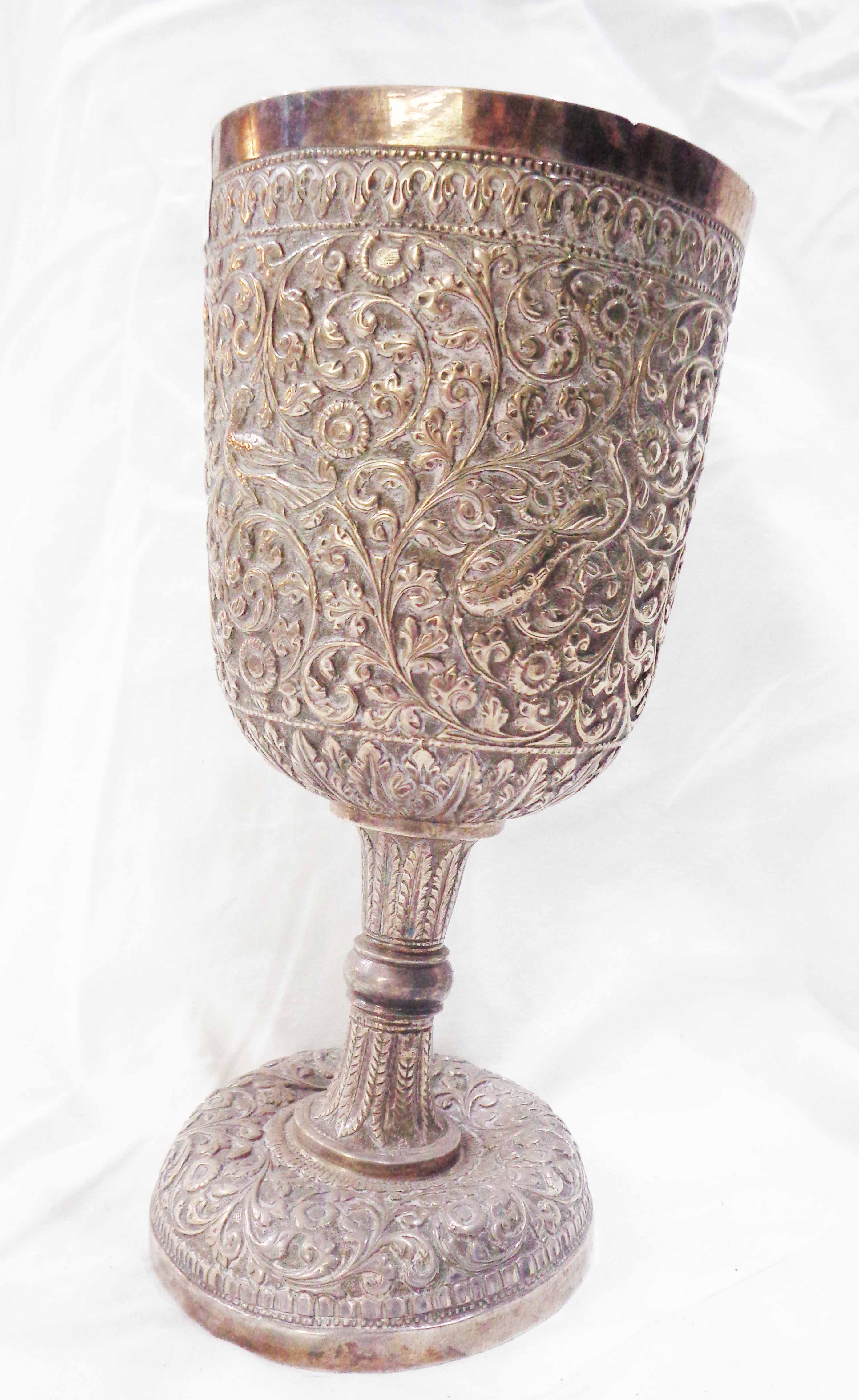 A 17.5cm high Anglo-Indian white metal goblet with profuse embossed foliate scroll and perching