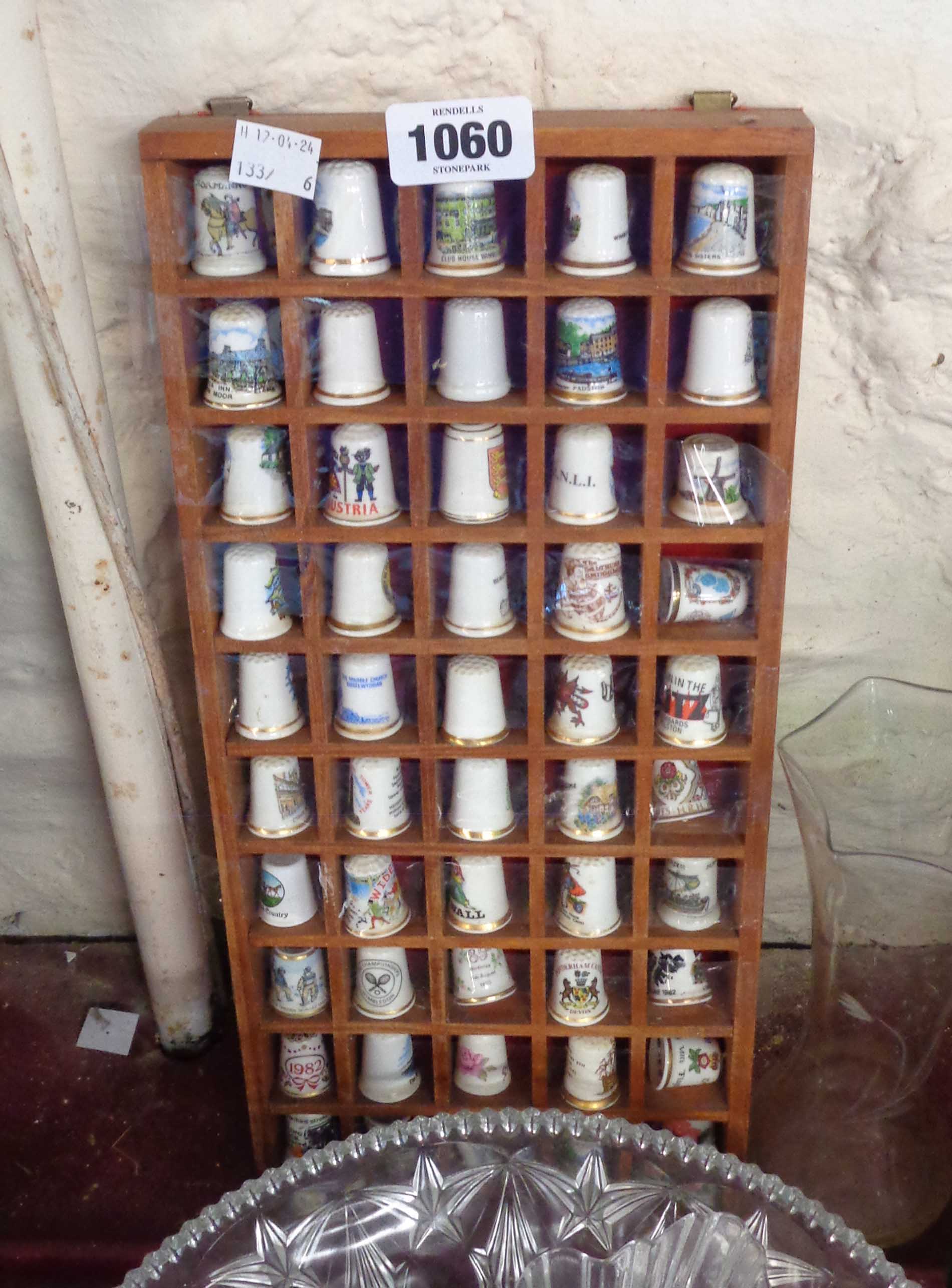 A small wooden display shelf containing a quantity of ceramic thimbles