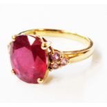 A marked 9k yellow metal ring, set with central oval heat treated ruby and flanking tiny pink stones