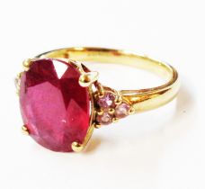 A marked 9k yellow metal ring, set with central oval heat treated ruby and flanking tiny pink stones