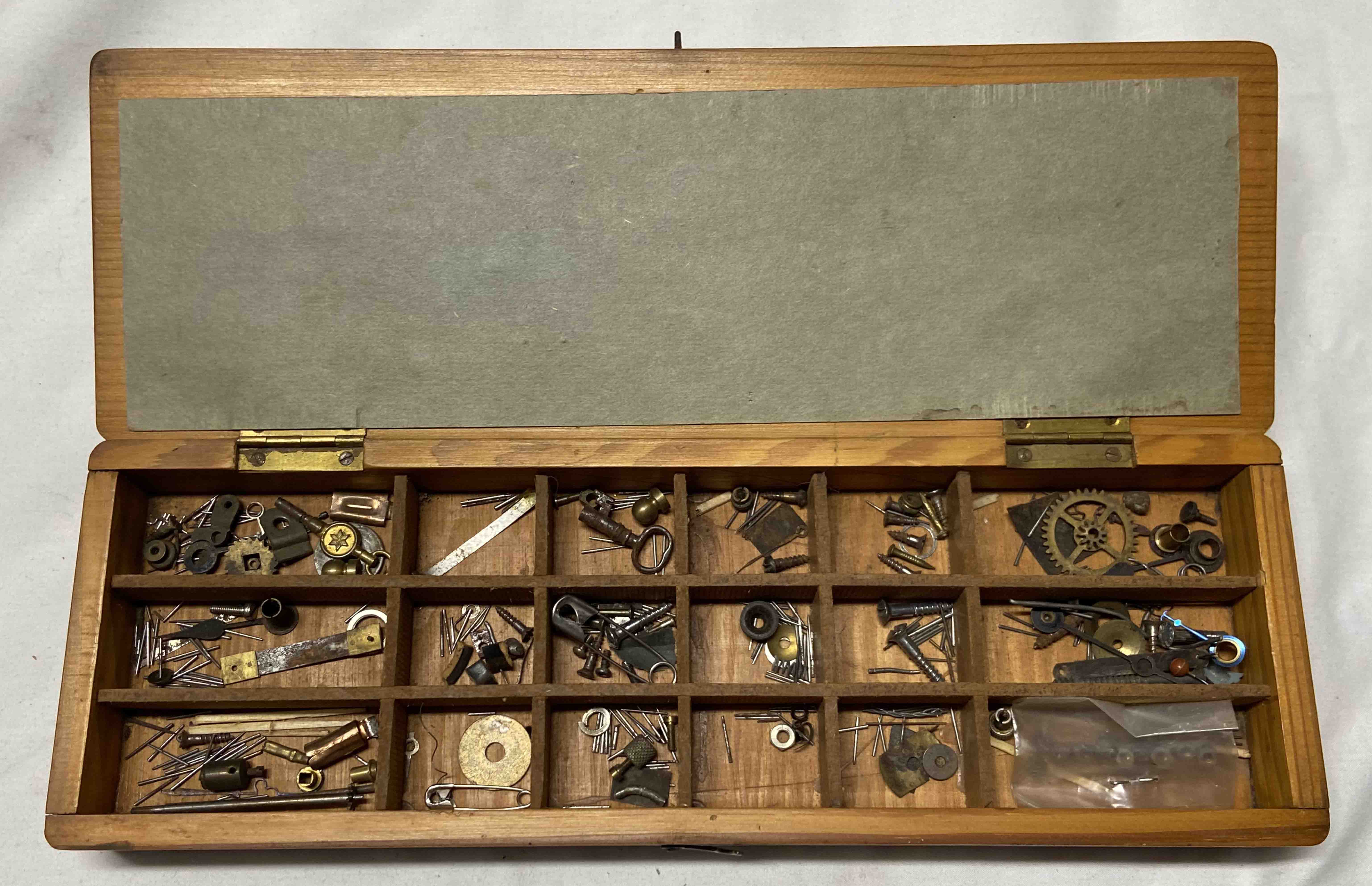 A vintage wooden box with interior compartments containing clock and watch making components