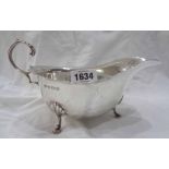 A Birmingham silver gravy boat with shaped rim and scroll handle, set on triple hoof pattern feet