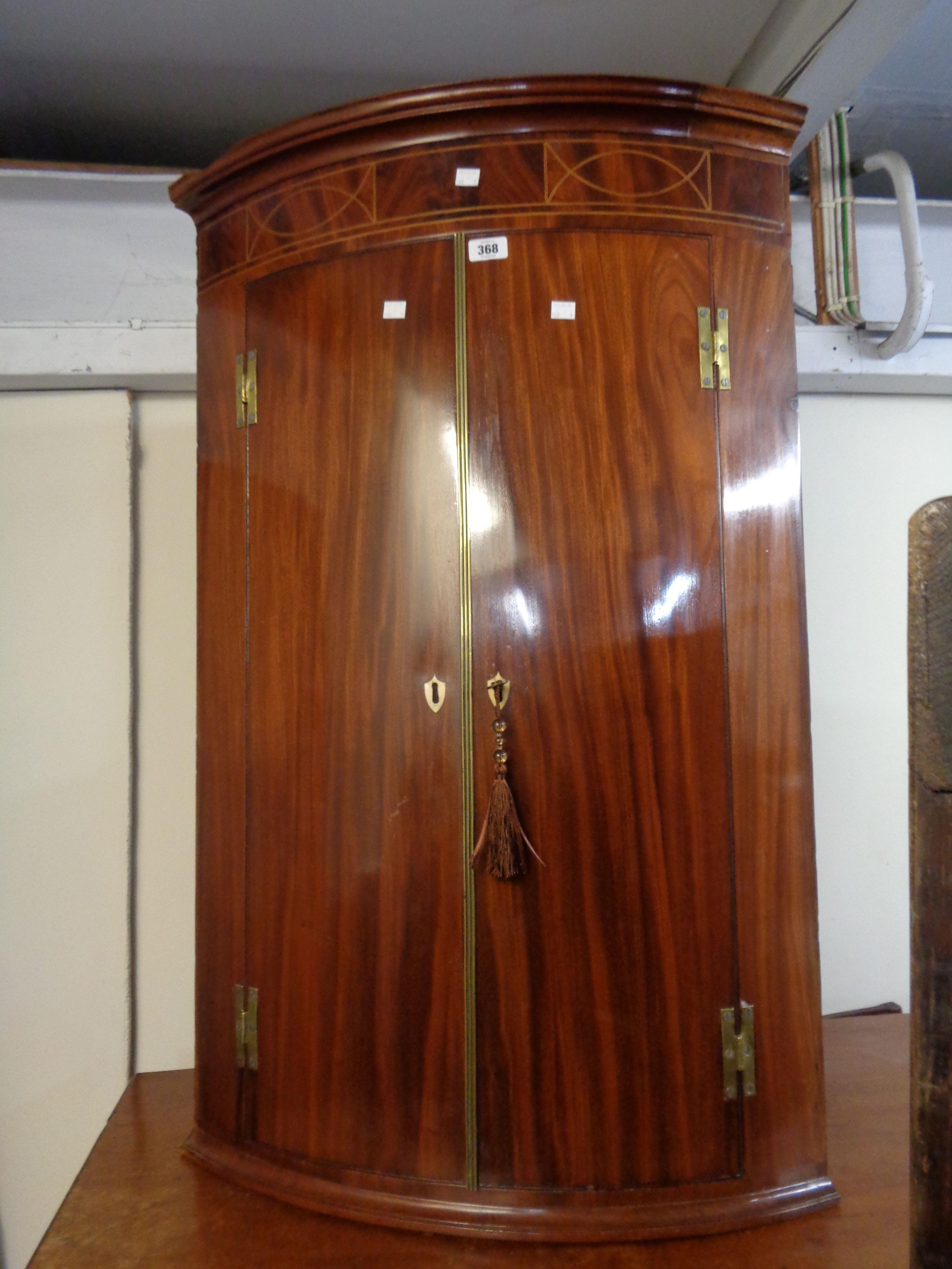 A 71cm late Georgian mahogany and strung wall mounted bow front corner cabinet with shelves enclosed
