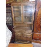 A 98cm Ercol dark elm two part wall unit with shelves enclosed by a pair of glazed panel doors