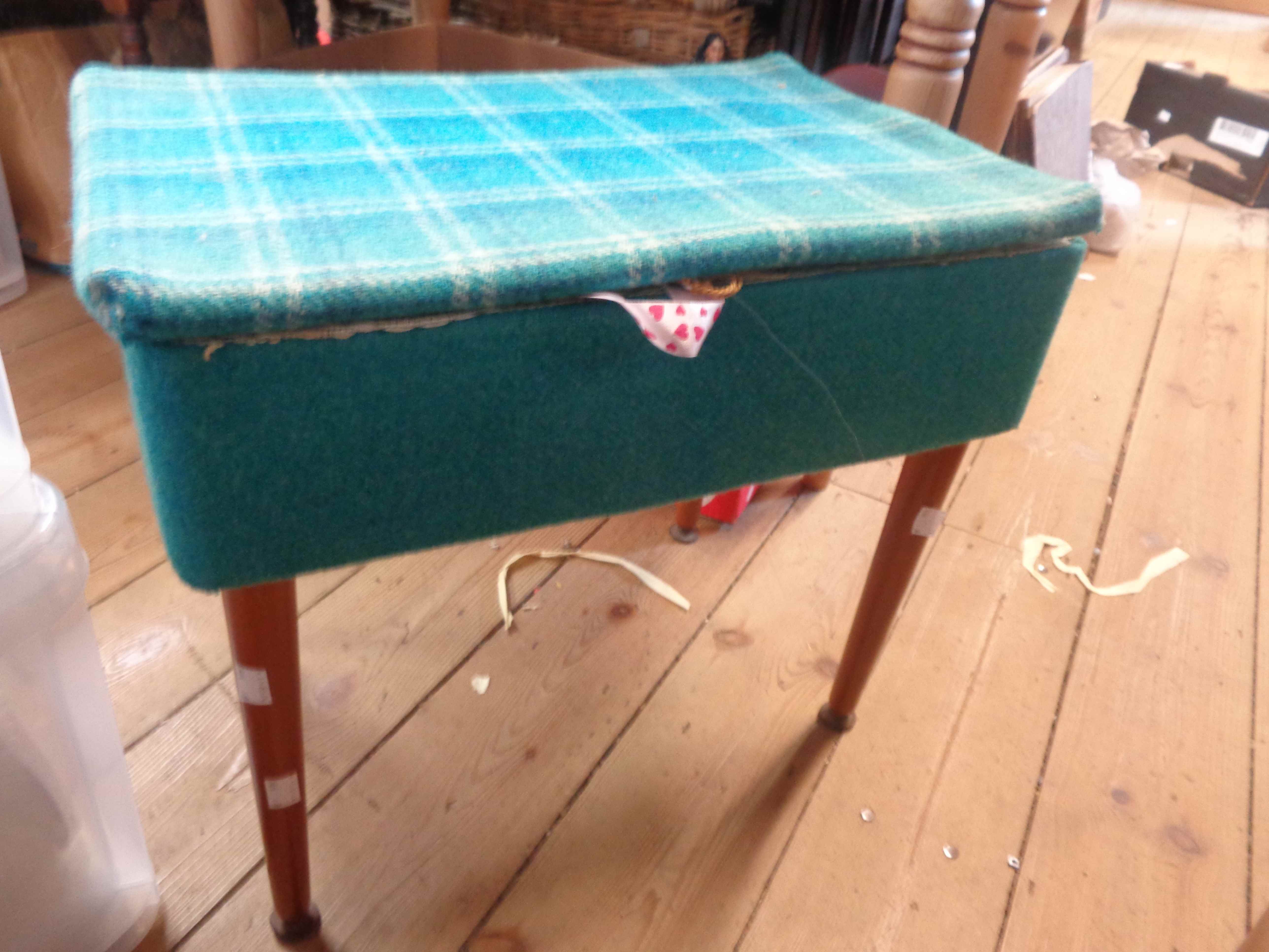 A vintage blue material upholstered lift-top sewing box with assorted contents, set on tapered