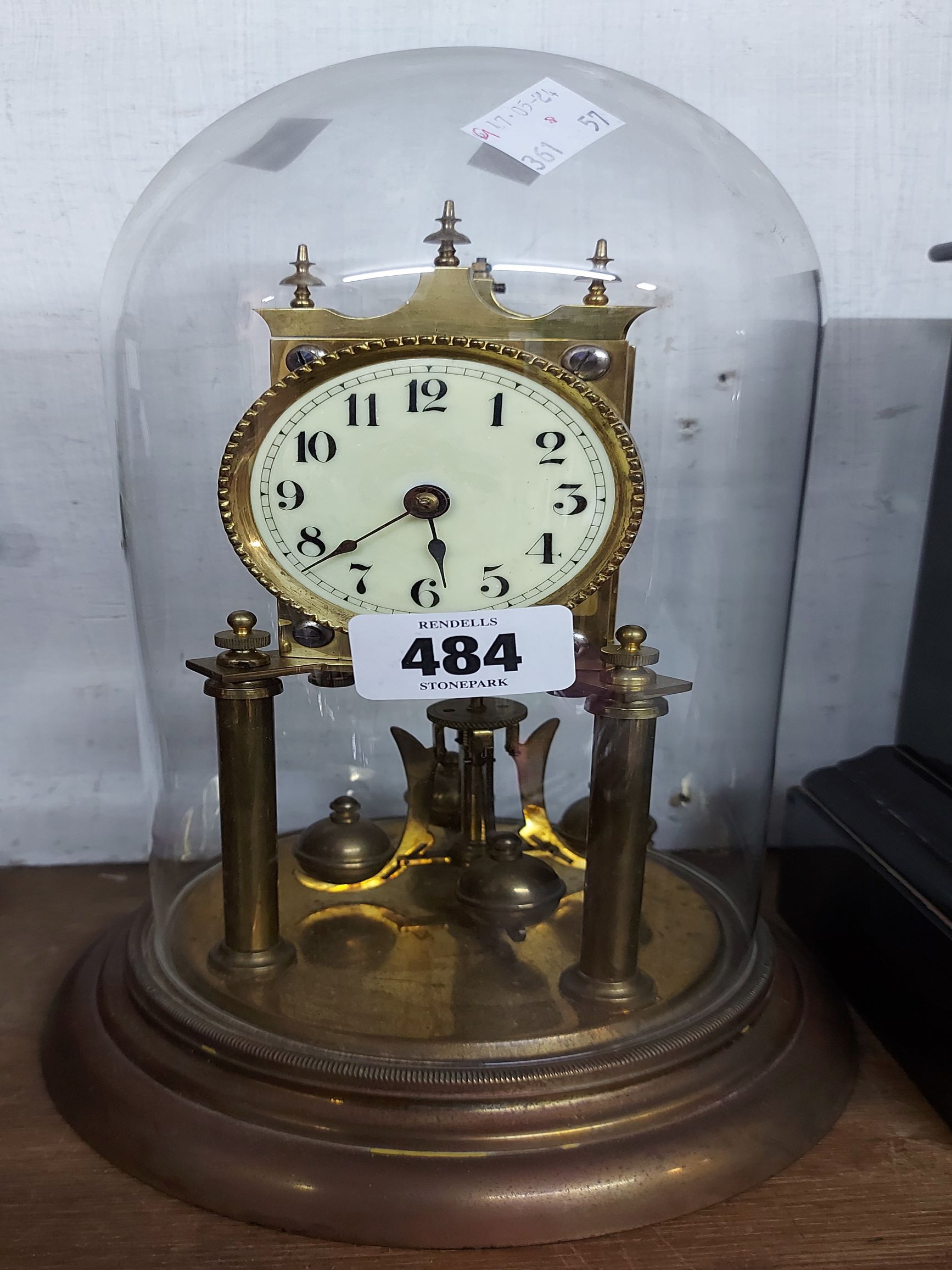A vintage brass anniversary clock with Arabic numerals and ball pendulum, under a glass dome