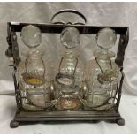 A vintage silver plated tantalus with scrolling foliate decoration containing three decanters each