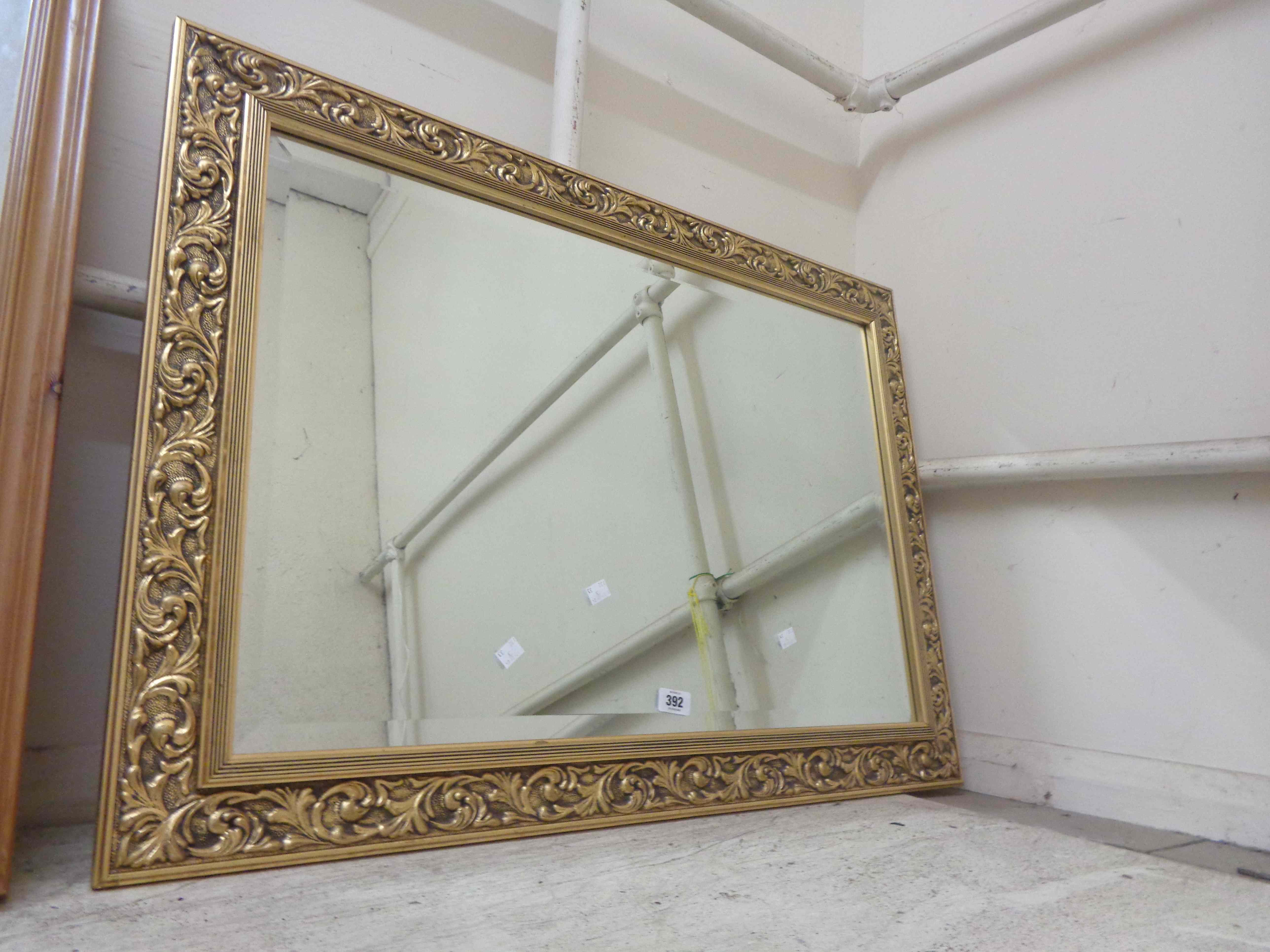 A large modern gilt framed bevelled oblong wall mirror with floral scroll border