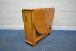 A 20TH CENTURY OAK DROP LEAF TABLE, the single door enclosing four folding nesting chairs, open