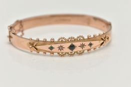 A 9CT GOLD EDWARDIAN BANGLE, rose gold hinged bangle, set with three green stones assessed as two