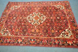 A RED WOOLEN PERSIAN RUG, with geometric patterns, central medallion, and multi strap border,