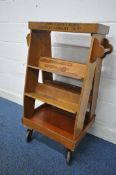 AN EARLY 20TH CENTURY OAK BOOK TROLLEY, fitted with an arrangement of six shelves, a small storage
