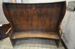 A GEORGIAN ELM CURVED BACK SETTLE, the seven panel back flanked by wavy sides and open armrests,
