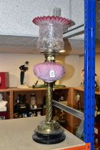 A TALL VICTORIAN BRASS OIL LAMP, with a pink glass reservoir, clear to cranberry frilled shade,