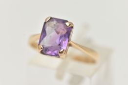A YELLOW METAL GEM SET RING, rectangular cut purple stone assessed as amethyst, prong set in