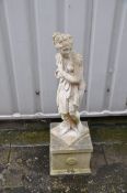 A WEATHERED COMPOSITE GARDEN FIGURE OF A SCANTILY CLAD WOMAN on a square base measuring width 30cm x