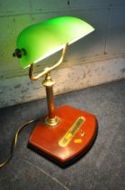 A BRASS BANKERS LAMP, with a green adjustable shade, on a wooden base fitted with a pen tray