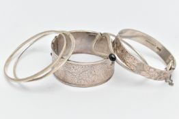 THREE SILVER BANGLES AND TWO WHITE METAL BANGLES, the first a silver wide hinged bangle, with