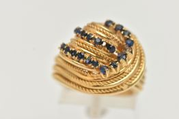 A YELLOW METAL GEM SET RING, a knot design dress ring, set with nineteen circular cut blue stones,