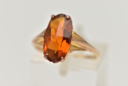 AN ORANGE PASTE RING, designed as an oval orange paste in a four claw setting to the tapered