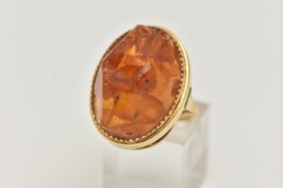 A PRESSED AMBER RING, designed as a large oval piece of pressed amber within a collet style setting,
