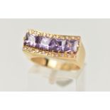 A YELLOW METAL DRESS RING, a rectangular form mount with concave detail, set with four purple square