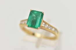 A YELLOW METAL EMERALD AND DIAMOND RING, centering on an emerald cut emerald, measuring